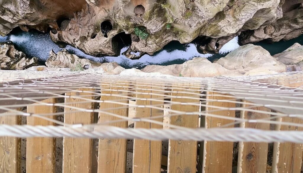 Uitzicht tussen de houten planken van de loopbrug naar de rivier de Guadalhorce diep beneden
